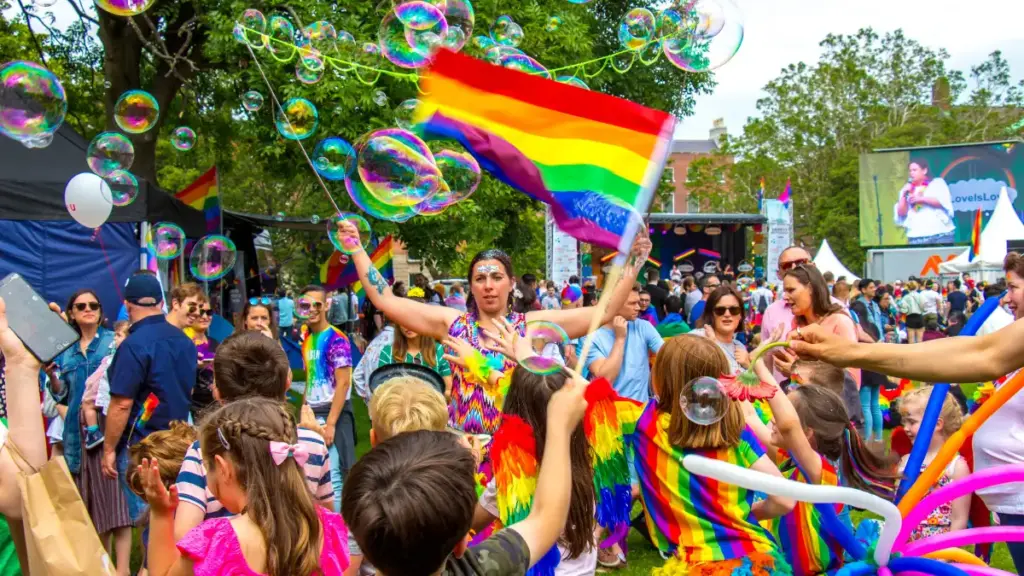 Celebrazione del Pride in un parco con bandiere arcobaleno, bolle di sapone e una folla festante