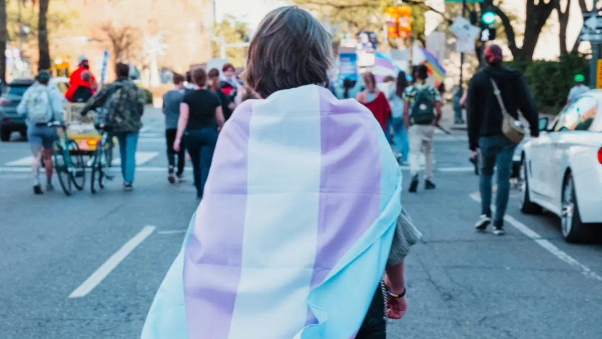 Partecipante a una marcia per i diritti civili cammina per strada portando sulle spalle la bandiera dell'orgoglio transgender