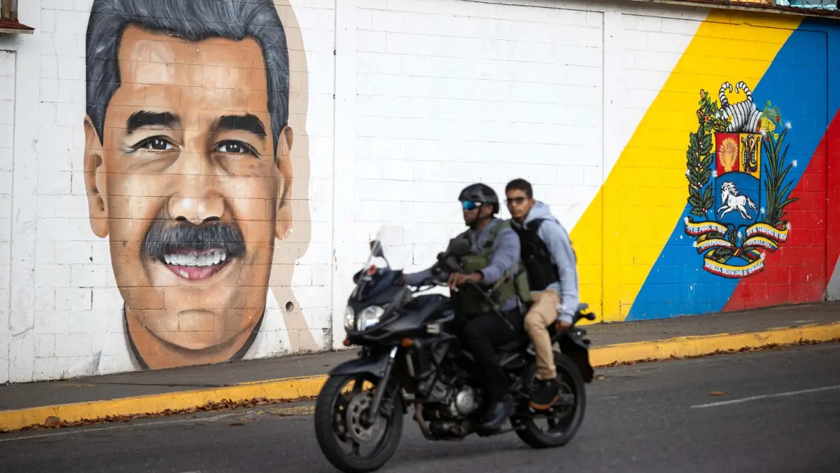 Due uomini in moto passano davanti a un murale che raffigura l'ex dittatore Nicolas Maduro in una strada di Caracas, capitale del Venezuela