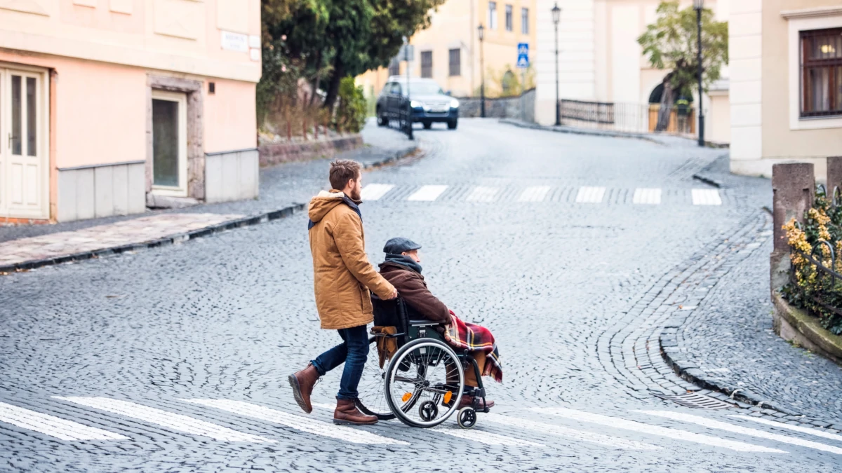 Anziano in carrozzella spinta da un giovane caregiver