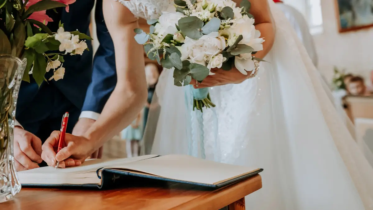 Dettaglio del momento della firma del registro durante un matrimonio religioso, con sposi e bouquet di fiori in primo piano