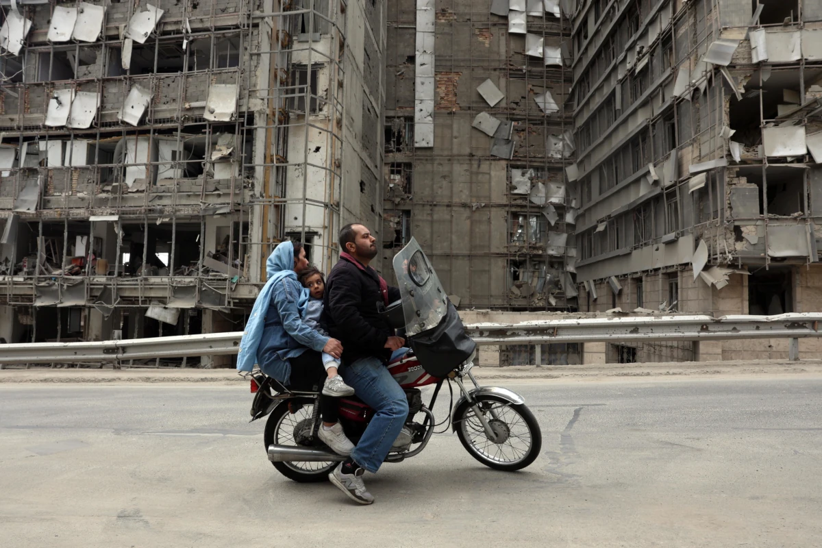 Una famiglia davanti all’Ospedale Gandhi a Teheran danneggiato dai bombardamenti israelo-americani, 2 marzo 2026 (foto Ansa)