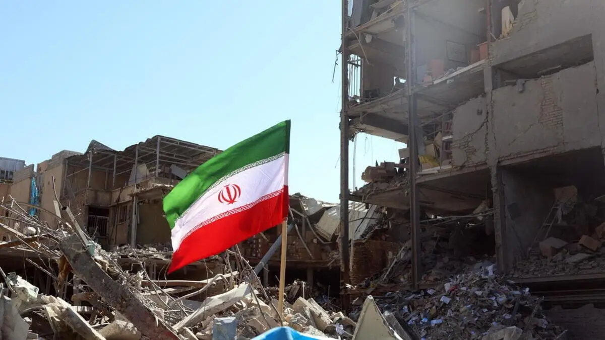 Una bandiera della Repubblica islamica sventola di fianco a un palazzo distrutto dai bombardamenti a Teheran, in Iran
