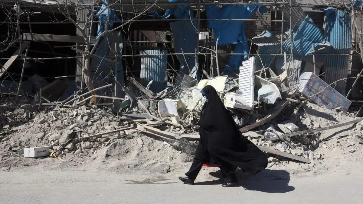 Una donna velata cammina di fianco a un palazzo distrutto dai bombardamenti a Teheran, in Iran