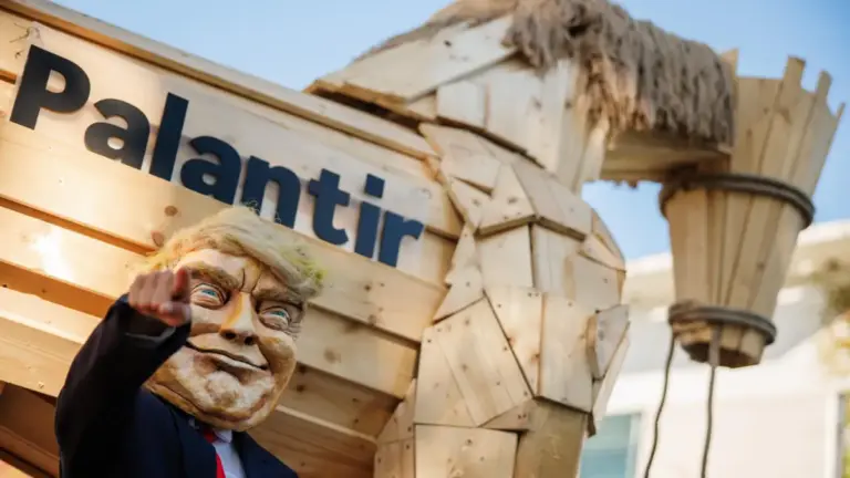 Un attivista indossa la maschera di Donald Trump di fronte a un "cavallo di Troia" con la scritta Palantir, durante una protesta in Germania in 3 settembre 2025