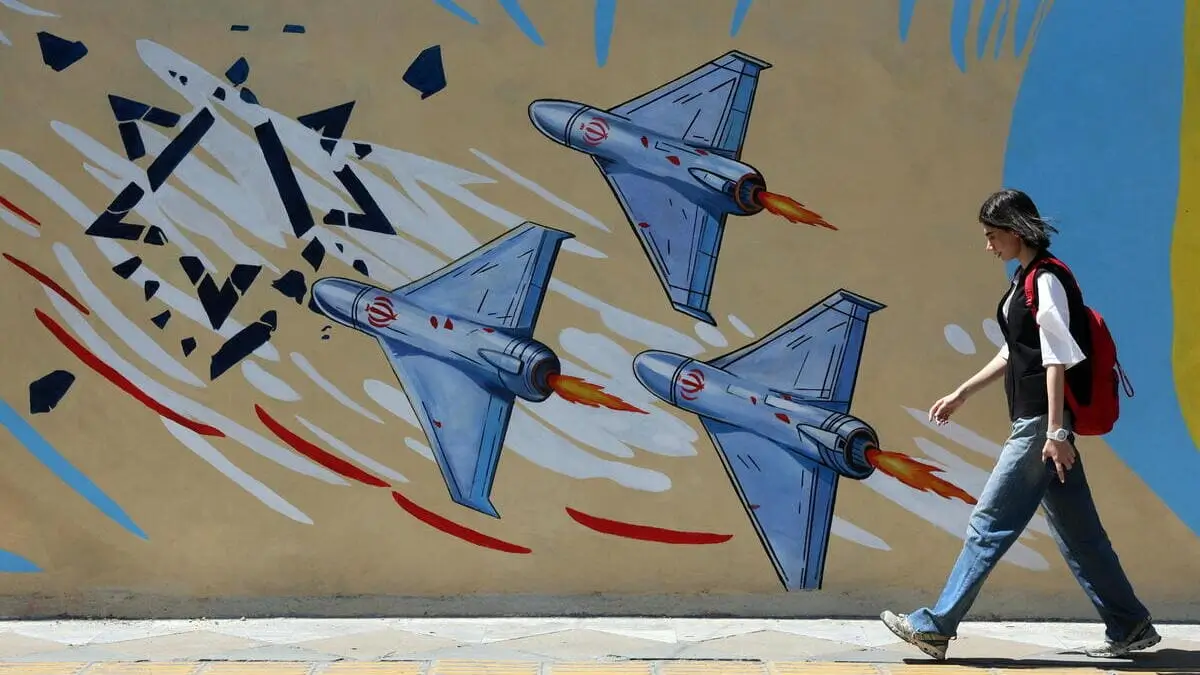 Una ragazza cammina a Teheran di fianco a un murale di propaganda anti-israeliana in Iran