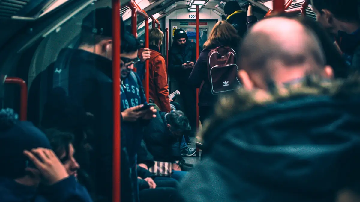Persone in piedi e sedute all’interno di una metropolitana, molte guardano lo smartphone mentre il vagone è affollato